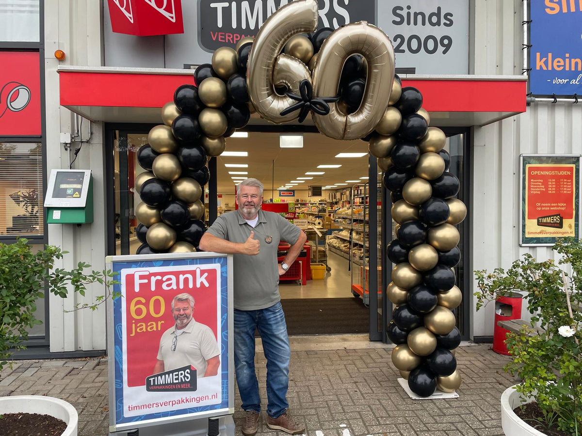 Frank van Kleinkantoor wordt 60 jaar bij de entree van de winkel met gouden ballonnenboog